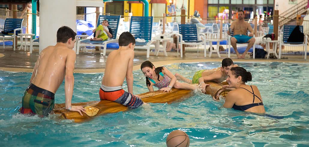 Kids playing on floating log in activity pool at indoor waterpark