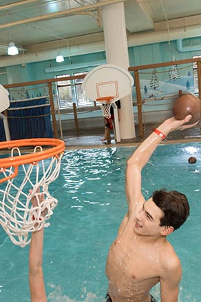 Boy dunking basketball in activity pool at water park