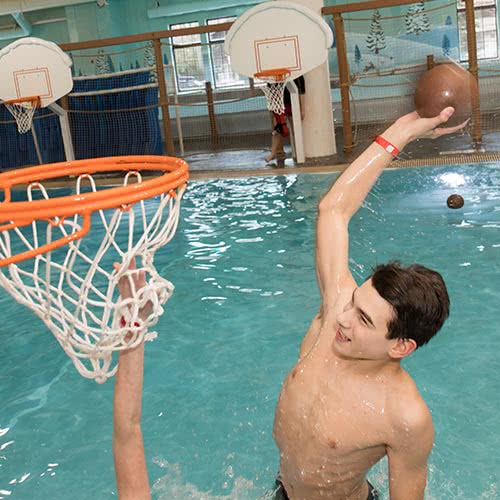 Boy dunking ball in basketball hoop i a pool at indoor water park